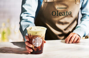Barista in brown apron with "Oleato" hands off a Starbucks Oleato Golden Foam Cold Brew