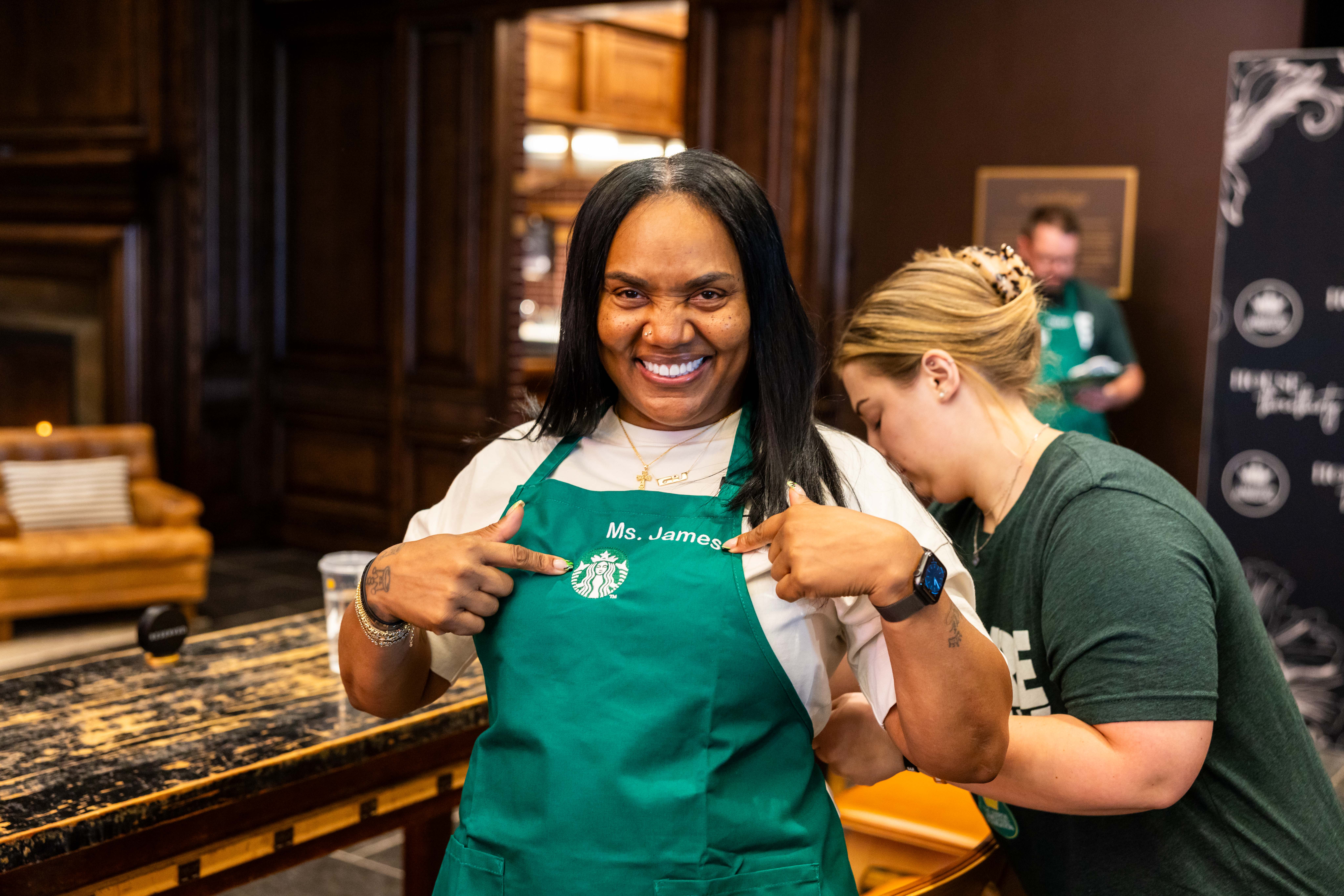 Smiling barista pointing at Starbucks logo on apron
