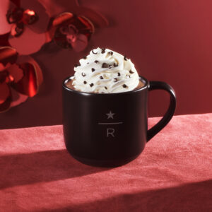 Starbucks Reserve mug containing beverage topped with whipped cream and chocolate shavings, on a red tablecloth with red backdrop.