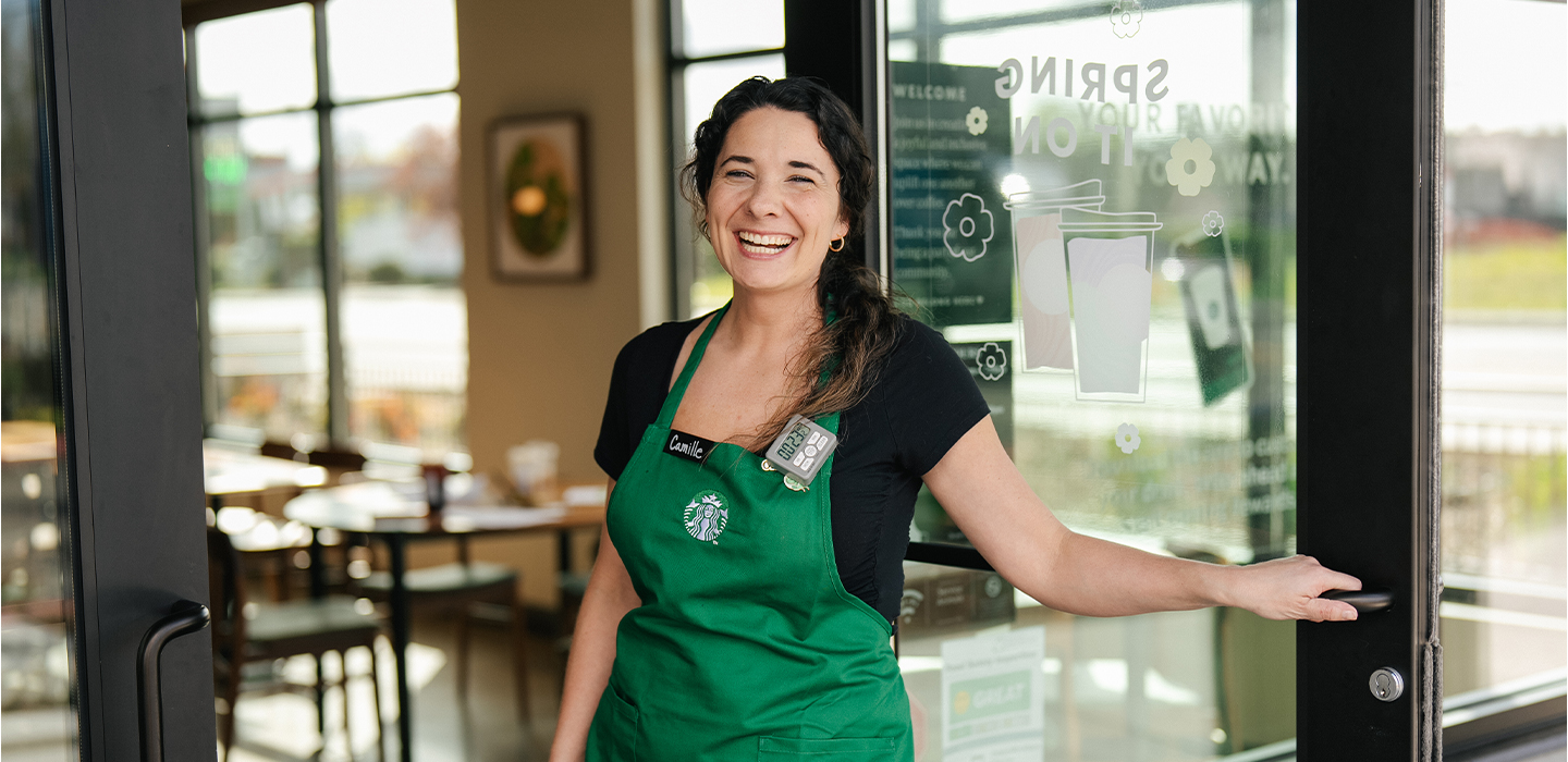 Smiling woman barista opens the door to Starbucks cafe