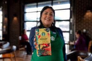 A Starbucks barista wearing a green apron and holding a Starbucks Ethiopia coffee bag