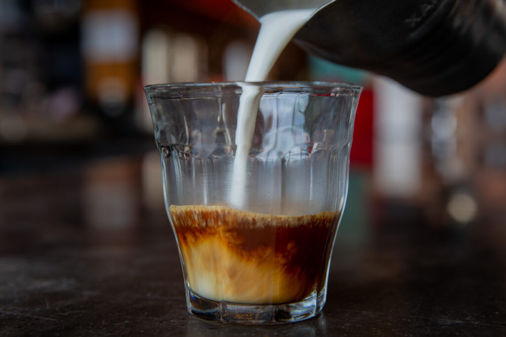 A small glass containing espresso shot and milk being poured into it