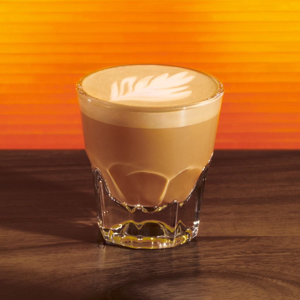 Starbucks hot honey cortado in a small glass on an orange background