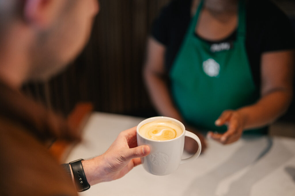 A Starbucks barista handing a latte in for here mug to a customer