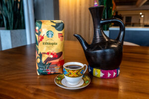 A Starbucks single origin coffee bag next to a small cup of coffee and an Ethiopian black clay coffee brewer