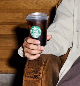 Man's hand on arm of chair holding Starbucks iced coffee in a cup