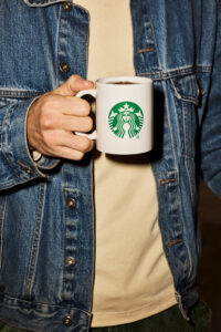 Man's torso in jean jacket, holding a Starbucks ceramic mug full of coffee