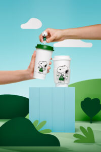 Two hands reaching out to two reusable cups for Starbucks and Peanuts collaboration