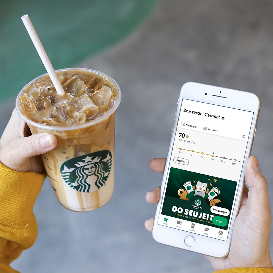 Person holds an iced coffee in one hand and a cell phone with Starbucks Rewards displayed on screen in the other